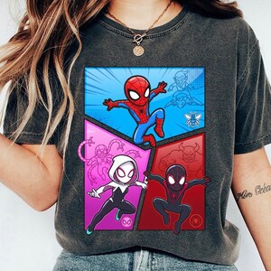May include: Dark gray t-shirt featuring a colorful comic-style graphic of Spider-Man and other characters. The design includes Spider-Man in a blue and red suit, and other characters in a comic book style.