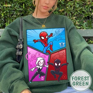 May include: Forest green sweatshirt featuring a comic book style graphic of Spider-Man and other characters. The graphic is divided into four panels with a blue, pink, and red background. The sweatshirt has a round neckline and long sleeves.