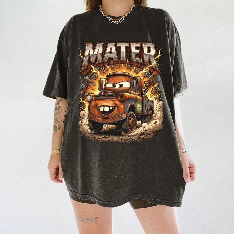 May include: Black t-shirt featuring a graphic of Mater from the movie Cars. The design includes the word "MATER" in a bold, metallic font above the cartoon truck. The image has a distressed, vintage look.