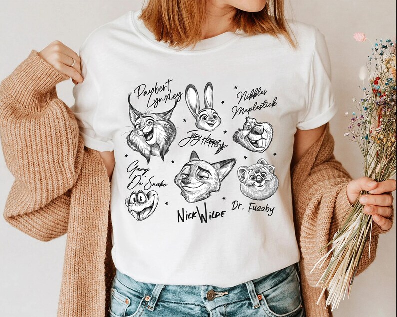Puede incluir: Camiseta blanca con ilustraciones en blanco y negro de personajes de dibujos animados de animales. La camiseta presenta personajes como un lince, un conejo, un zorro y un oso, cada uno con sus nombres escritos encima o debajo.