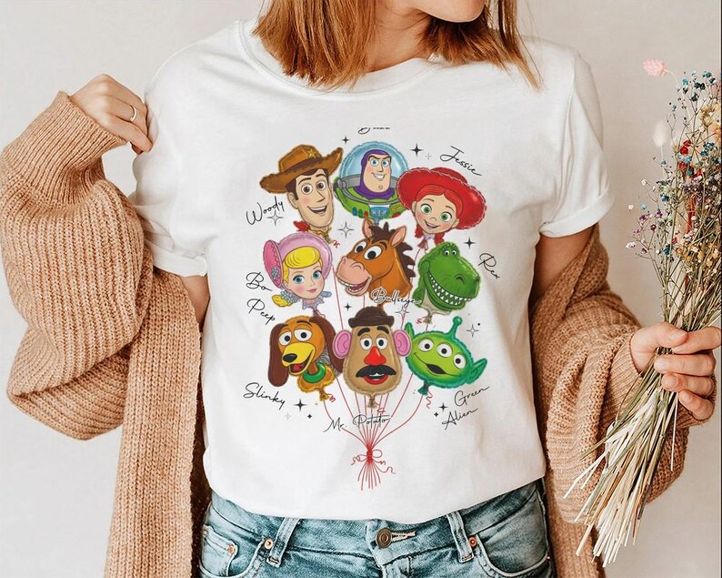 Puede incluir: Camiseta blanca con un gr&aacute;fico colorido de personajes de Toy Story como globos. El dise&ntilde;o incluye a Woody, Buzz Lightyear, Jessie y otros, con sus nombres encima. Un dise&ntilde;o alegre y juguet&oacute;n.