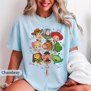 Puede incluir: Camiseta azul claro con un gr&aacute;fico de personajes de Toy Story como globos. El dise&ntilde;o incluye a Woody, Buzz Lightyear, Jessie, Bo Peep, Rex, Slinky, Mr. Potato Head y un Alien verde. La palabra "Chambray" est&aacute; en la esquina inferior izquierda.
