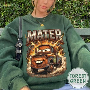 May include: Forest green sweatshirt featuring a graphic of Mater from the movie Cars. The word "MATER" is printed above the cartoon truck. The design includes lightning bolts and tools. The sweatshirt is a solid forest green color.