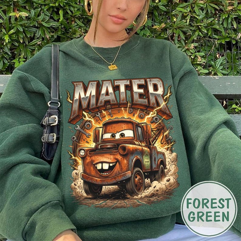 May include: Forest green sweatshirt featuring a graphic of Mater from the movie Cars. The word "MATER" is printed above the cartoon truck. The design includes lightning bolts and tools. The sweatshirt is a solid forest green color.