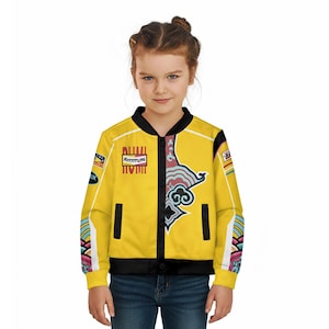 May include: A yellow bomber jacket with black trim and a colorful graphic design. The jacket features a front zipper, side pockets, and a ribbed collar and cuffs. The sleeves have a colorful pattern. The jacket has the word "Attitude" printed on it.