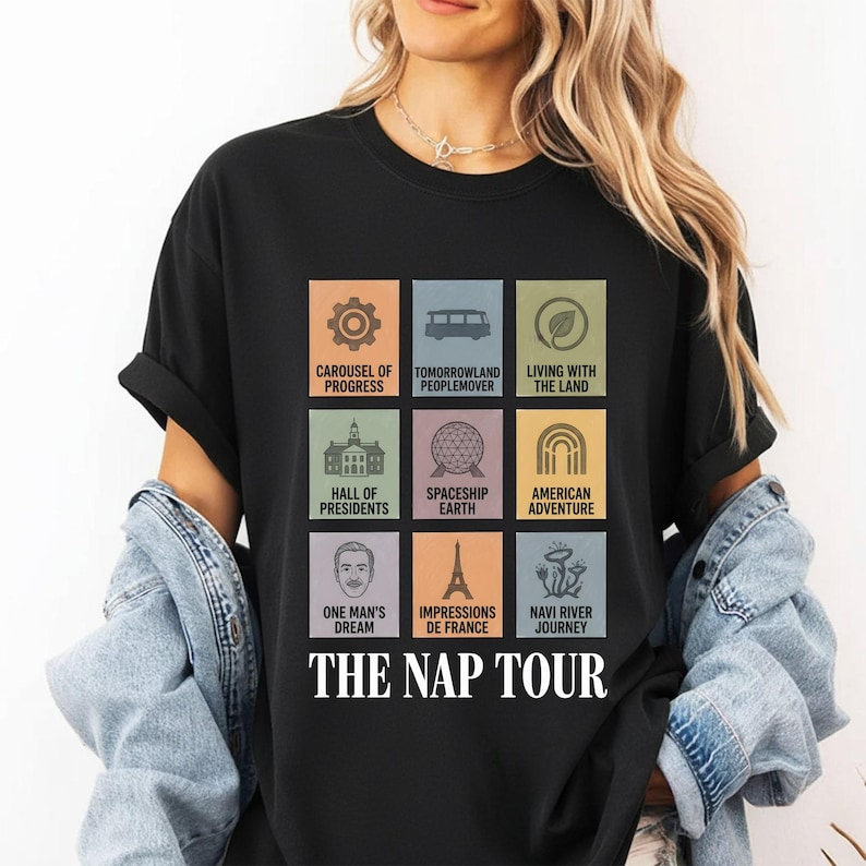 May include: Black t-shirt featuring colorful square graphics with text including "Carousel of Progress," "Tomorrowland Peoplemover," and "The Nap Tour." The design includes icons and text related to theme park attractions.
