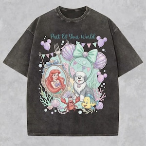 May include: A charcoal gray acid-wash t-shirt featuring a graphic print with the text Part Of Your World. The design includes a mermaid, a dog, a crab, and a fish surrounded by seashells, balloons, and a bow, all in pastel colors.