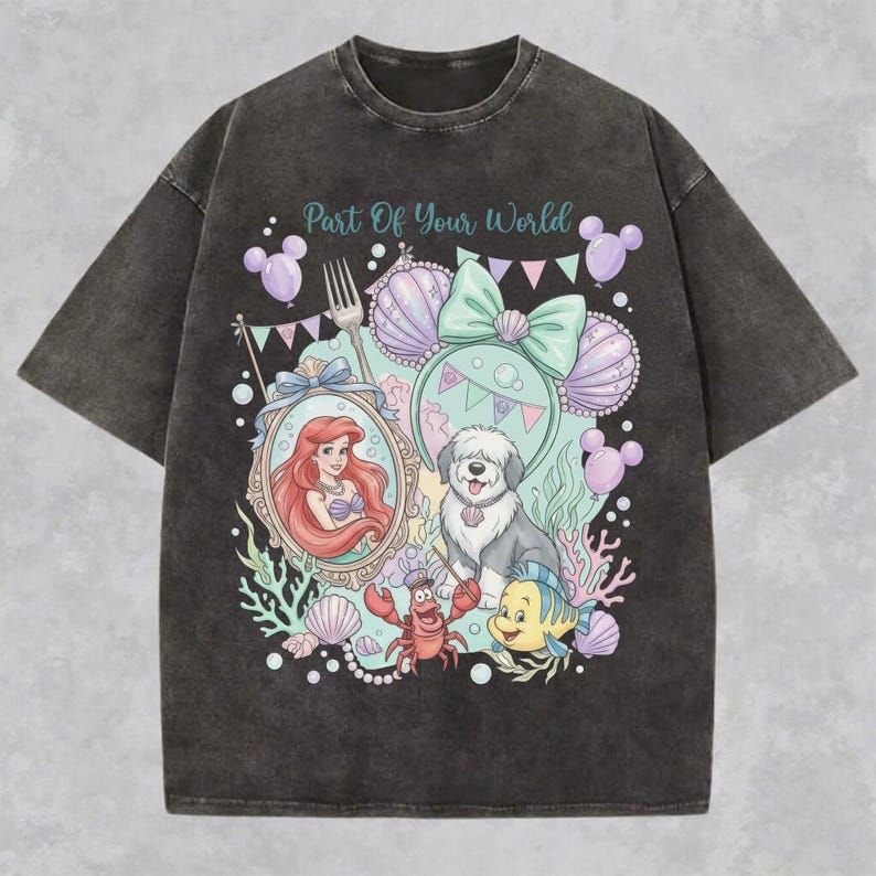 May include: A charcoal gray acid-wash t-shirt featuring a graphic print with the text Part Of Your World. The design includes a mermaid, a dog, a crab, and a fish surrounded by seashells, balloons, and a bow, all in pastel colors.