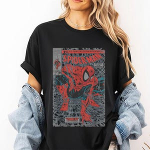 Pode incluir: Uma t-shirt preta de manga curta com uma impress&atilde;o gr&aacute;fica de uma capa de banda desenhada vintage do Spider-Man. A ilustra&ccedil;&atilde;o mostra a personagem num fato vermelho e azul agachada sobre um fundo de teia com o texto Spider-Man e Torment.