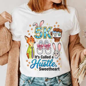 May include: White t-shirt with a Zootopia-themed design. It features the text "5K" and "It's Called a Hustle, Sweetheart", alongside cartoon characters, running shoes, paw prints, and a Springtime Surprise 2020 badge.