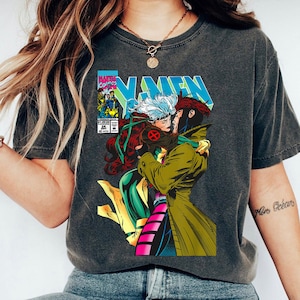 May include: Dark gray t-shirt featuring a comic book illustration of X-Men characters Rogue and Gambit embracing. The design includes the X-Men logo and Marvel Comics branding. The shirt has a vintage, worn look.