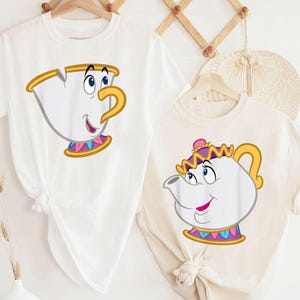 May include: Two white t-shirts featuring cartoon illustrations of the character Chip from Beauty and the Beast. One shirt has Chip's face, the other has Mrs. Potts. Both designs have yellow, blue, pink, and purple accents.