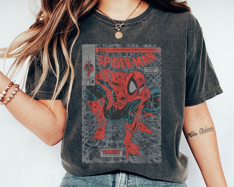 Pode incluir: Uma t-shirt cinzento-carv&atilde;o de manga curta com um gr&aacute;fico de capa de banda desenhada vintage do Spider-Man. A impress&atilde;o mostra a personagem vermelha e azul numa pose agachada com o texto Spider-Man, Torment e The Legend of the Arachknight.