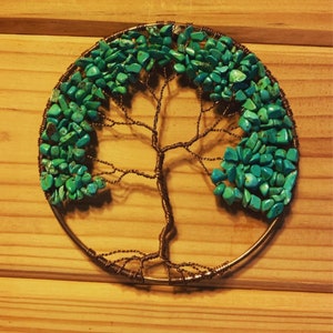 May include: A handcrafted copper wire tree sculpture with turquoise stone leaves. The tree is set within a circular frame, creating a unique wall art piece. The sculpture is displayed on a wooden surface.