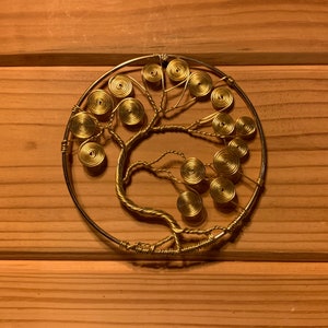 May include: A gold wire sculpture of a tree with a circular frame. The tree has a thick trunk and many branches with small, round leaves.