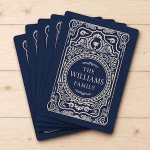May include: A stack of rectangular navy blue cards featuring a cream-colored ornate border and decorative scrollwork. The center of each card displays the text THE WILLIAMS FAMILY enclosed within a circular frame, topped by a small trophy icon.