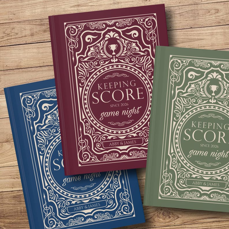 May include: Three hardcover books with ornate covers. The books are in shades of blue, burgundy, and green. Each book features the text "KEEPING SCORE game night" in a circular design, with the names "ABBY & JAMES" at the bottom.