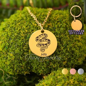 May include: A gold-coloured pendant necklace featuring a snake design. The round pendant has a black snake illustration and the text "Jolly Fran Jewelry". A keychain option is also shown.