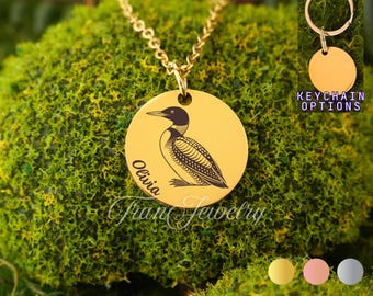 May include: Gold-colored pendant necklace with a detailed engraved loon bird design. The pendant has the name "Olivia" and the text "Fran Jewelry" engraved on it. A keychain option is also shown.