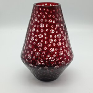 Könnte beinhalten: Eine rote Glasvase mit einem weißen Tupfenmuster. Die Vase hat die Form eines Kegels und eine breite Öffnung oben.