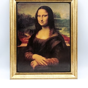 May include: A framed reproduction of the famous Mona Lisa painting. The painting features a woman with a soft smile, dark hair, and a brown dress. The frame is gold with a textured surface.