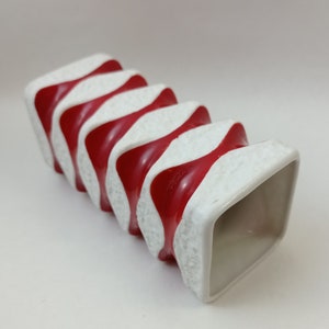 May include: White ceramic vase with red and white wavy stripes. The vase has a square opening and a textured surface.