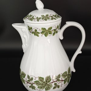 Peut inclure: Cafetière en porcelaine blanche avec un motif de vigne vert et brun. La cafetière a un couvercle avec un bouton en forme d'oiseau.