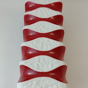 May include: A white ceramic vase with a red and white geometric pattern. The vase has a textured surface and a rounded shape.