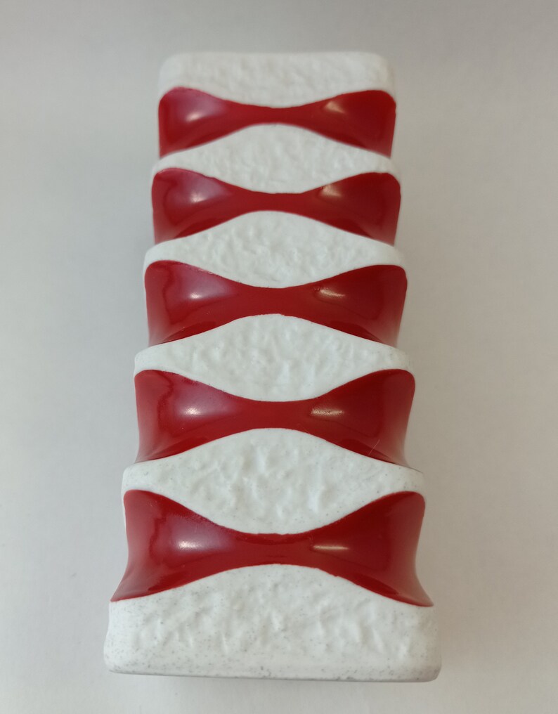 May include: A white ceramic vase with a red and white geometric pattern. The vase has a textured surface and a rounded shape.