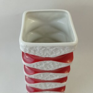 May include: White ceramic vase with red and white wavy stripes. The vase is tall and narrow.