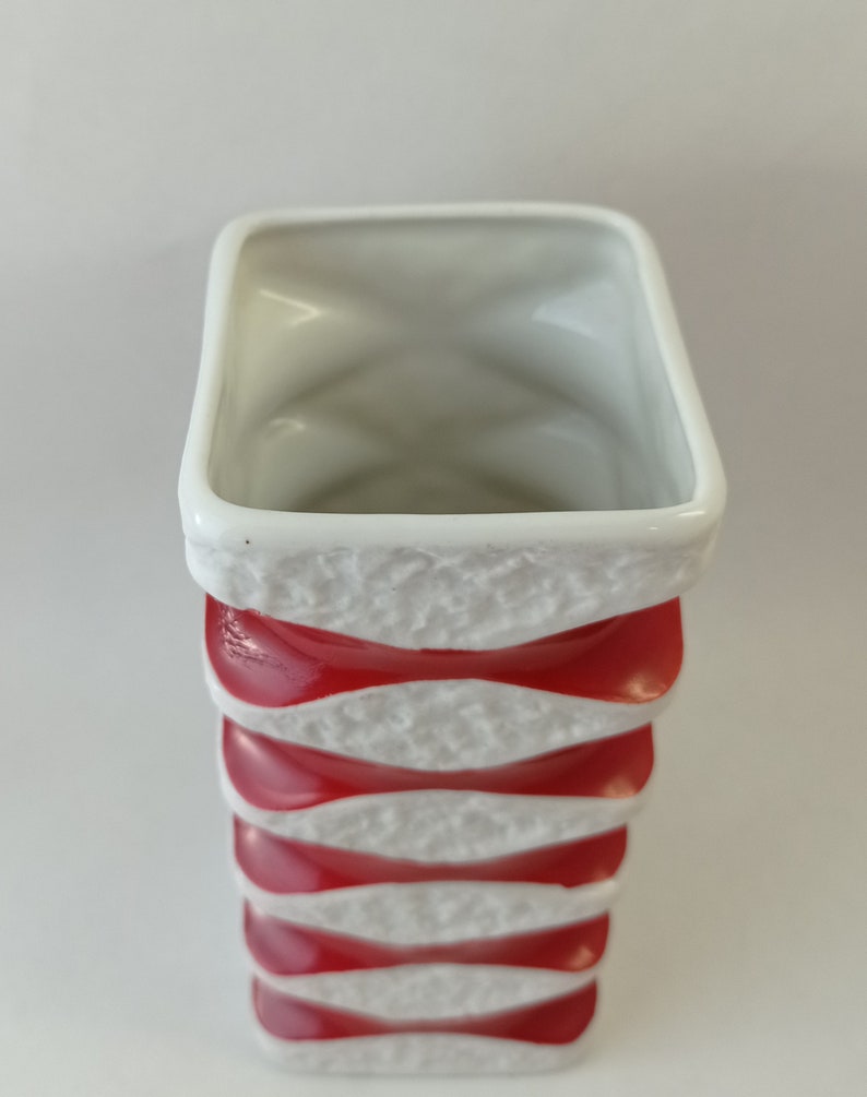 May include: White ceramic vase with red and white wavy stripes. The vase is tall and narrow.
