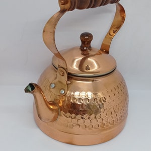 May include: A copper kettle with a hammered finish and a wooden handle. The kettle has a lid with a wooden knob.