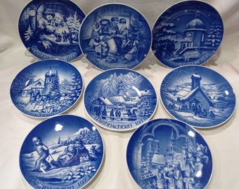 May include: Set of ten blue and white Christmas plates with a winter scene on each. The plates are decorated with a white border and the words "Weihnachten" and the year. The plates are all different and feature scenes such as a church, a village, and a forest.