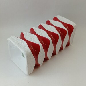 May include: A white ceramic vase with red wavy stripes. The vase has a textured surface and is shaped like a stack of squares.
