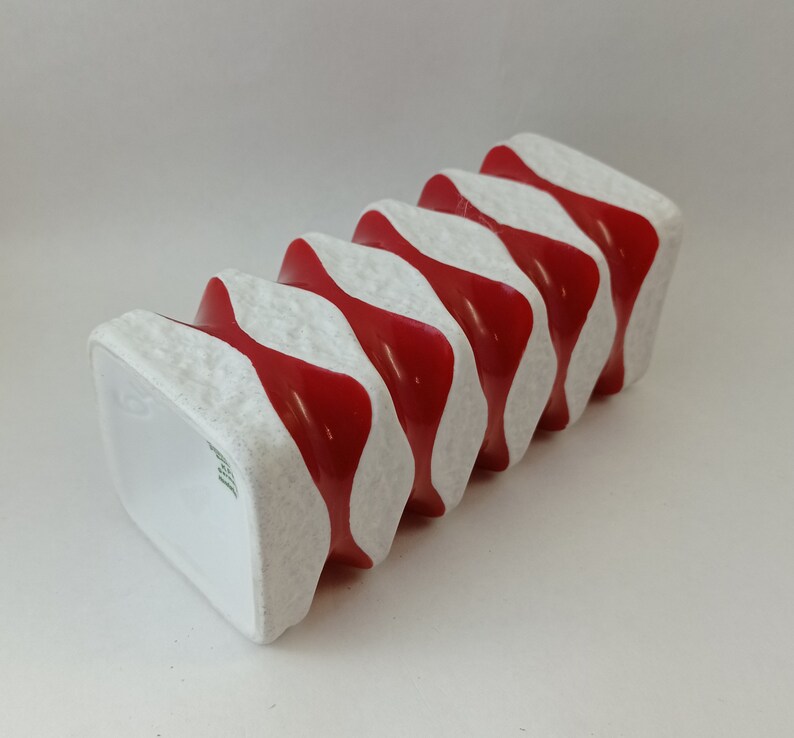 May include: A white ceramic vase with red wavy stripes. The vase has a textured surface and is shaped like a stack of squares.