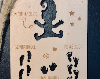 May include: Wooden craft template with cutouts for a silhouette of an elf, footprints, handprints, and a snowflake. The text "Schabernackschalohne" is at the top of the template. The text "Wichtel-Abdruck", "Schuhab-Druck", "Handabdruck", and "Fussabdruck" are also included.