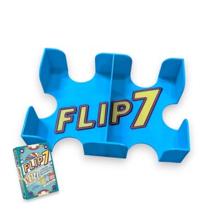 Op de afbeelding: Een blauwe plastic kaarthouder met het woord "FLIP7" erop gedrukt. De houder heeft meerdere vakken voor kaarten en is ontworpen om een ​​deck kaarten te houden.