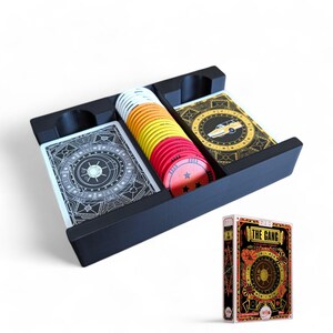 Könnte beinhalten: Ein schwarzer Plastik-Spielorganizer mit zwei Fächern für Karten und einem separaten Fach für Spielsteine. Der Organizer ist mit Karten und Spielsteinen gefüllt. Die Spielbox ist rot, gelb und schwarz mit dem Text "The Gang" auf der Vorderseite.