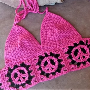May include: A pink crocheted halter top with black crocheted peace signs. The top is made with a fine yarn and has a delicate, feminine look.