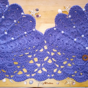 May include: A purple crocheted piece with a scalloped edge and pearl embellishments. The piece has a delicate, lacy design and is accented with a wooden button.
