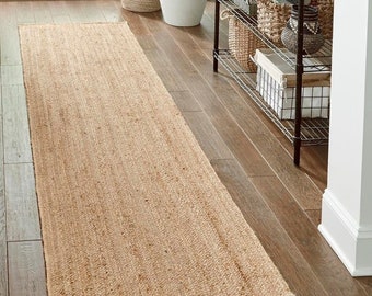 May include: A natural fiber runner rug in a light beige color. The rug is made of woven jute and has a textured surface. The rug is placed on a hardwood floor in a hallway.