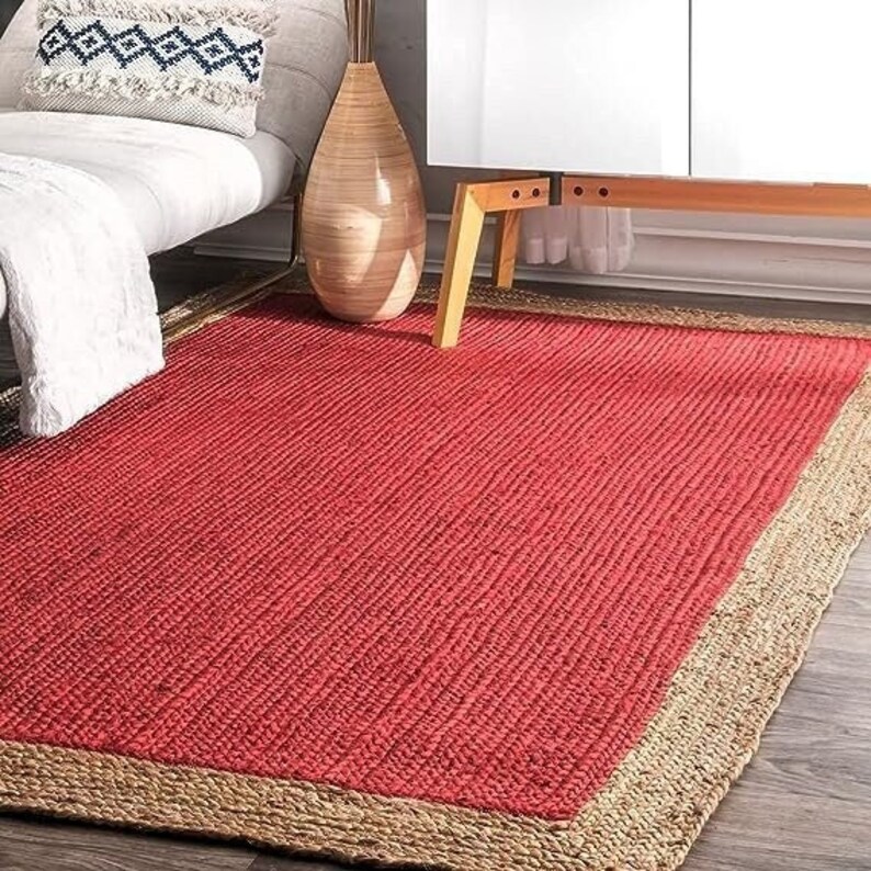 May include: A red and natural jute area rug with a woven texture and a natural jute border. The rug is on a hardwood floor.