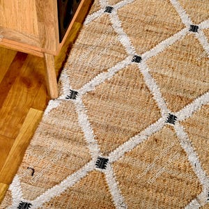 May include: A natural fiber rug with a geometric pattern in white and black. The rug is made of jute and has a hand-woven texture.