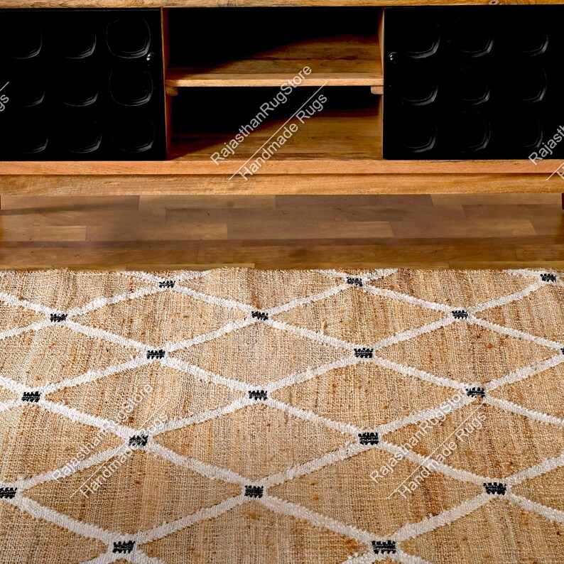 May include: A natural fiber rug with a diamond pattern in white and black. The rug is made of jute and is a natural, earthy color. The rug is shown in front of a wooden cabinet with black shelves.