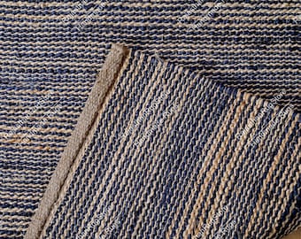 May include: A woven area rug featuring a striped pattern of alternating dark navy blue and natural tan fibres. The rug has a thick, textured surface with a visible braided weave construction and a folded corner revealing the underside texture.