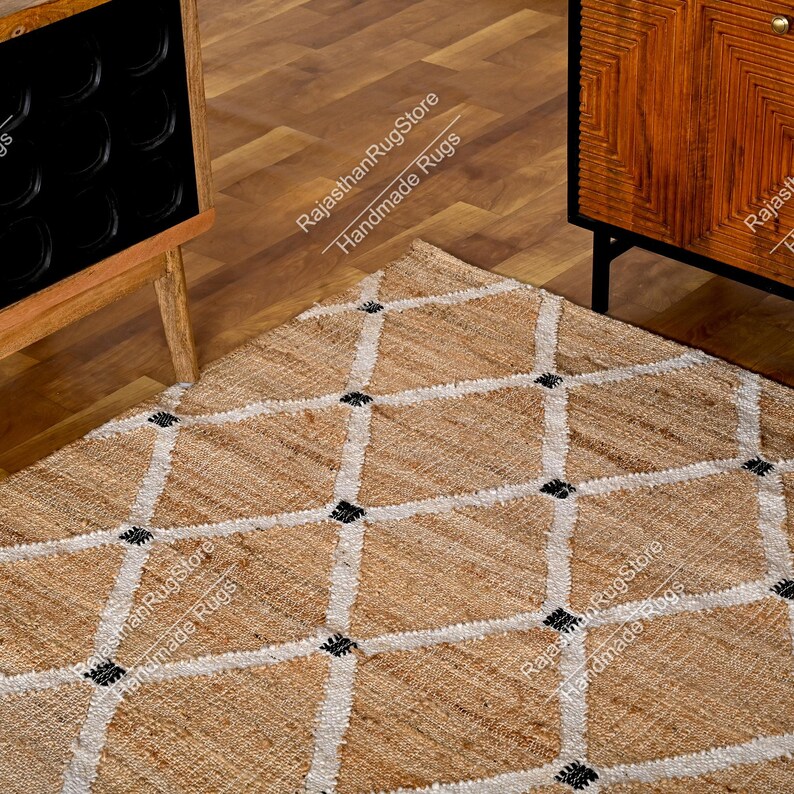 May include: A natural fiber rug with a diamond pattern in white and black. The rug is made of jute and is handmade. The rug is on a wooden floor.