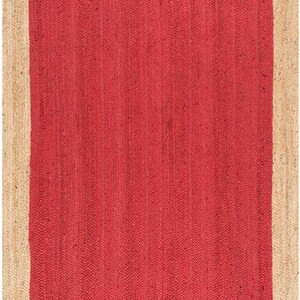 May include: A red jute rug with a natural jute border. The rug has a woven texture and a solid color.