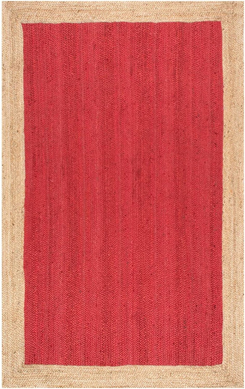 May include: A red jute rug with a natural jute border. The rug has a woven texture and a solid color.