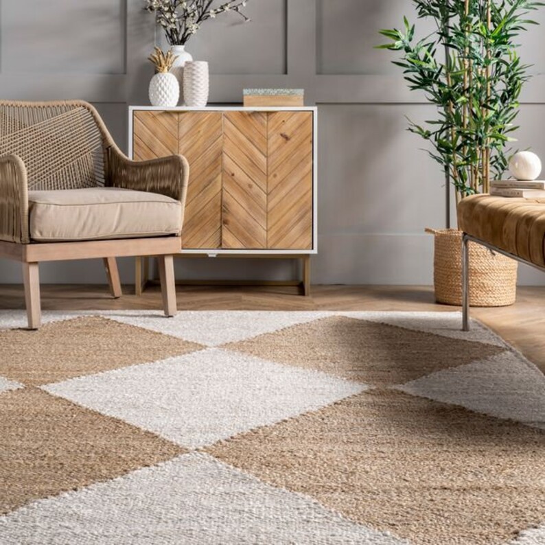 May include: A light brown and white checkered rug with a woven texture. The rug is in a living room setting with a chair, a cabinet, and a plant.