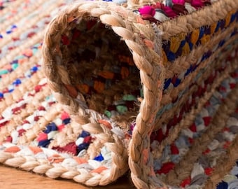May include: Close-up of a woven jute rug with colorful stripes and a braided edge. The rug is made of natural fibers and has a rustic, handmade look.